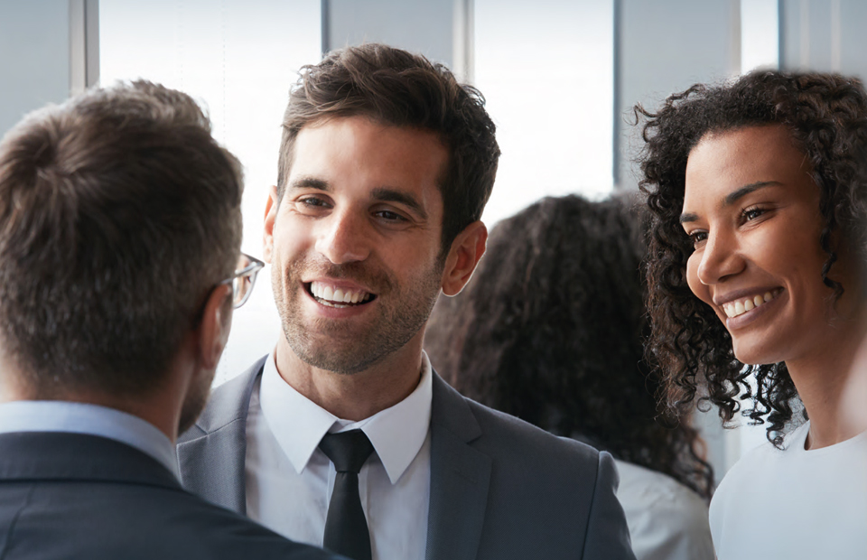 Picture shows two men and a woman with curly hair talking to and smiling at each other.