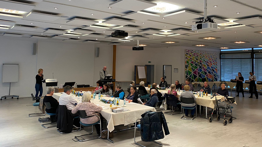 Photo shows room with two big tables where older people are sitting together