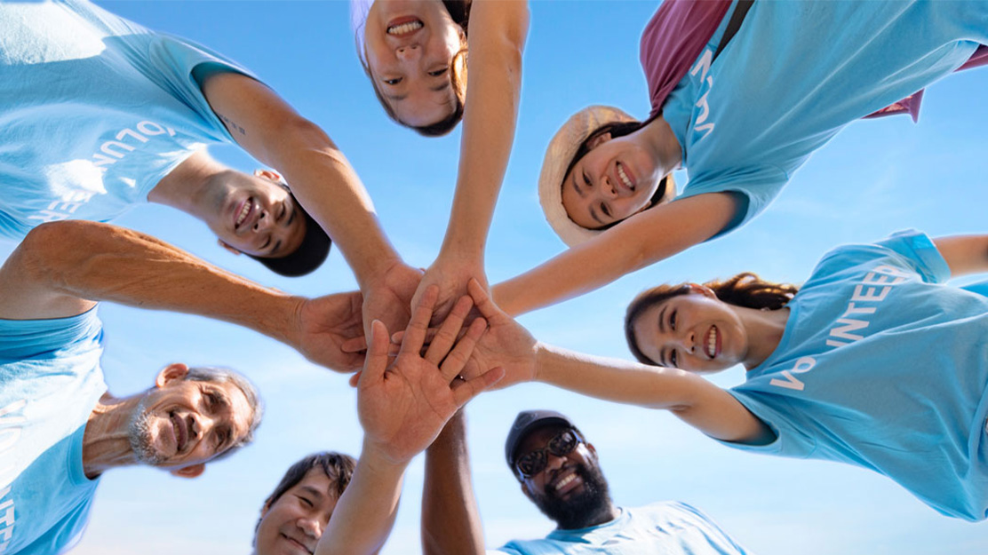 Photo shows a group of people putting their hands toegther and smiling into the camera