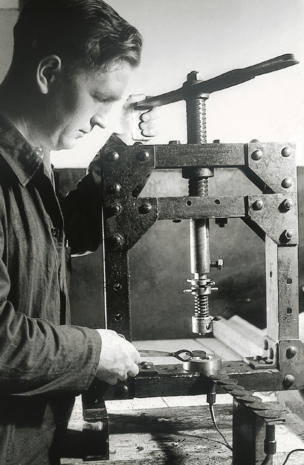 Historical photograph of a man operating a screw press to produce a seal