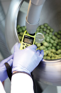 gloved hands hold a measuring device in a round steel container with green beads