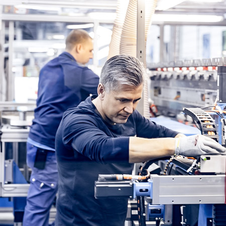 a worker in blue clothes working on a machine, another man in the background is also working on another machine