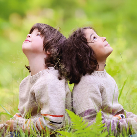 Picture shows two young children sitting back to back in the gras watching the sky.