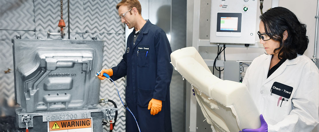 Two employees in protective gear operating technical equipment and inspecting components in a laboratory or production environment.