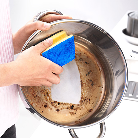 A dirty pot that is cleaned by a person using a yellow sponge
