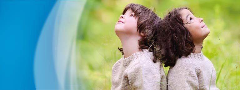 Two children sit back to back in the grass and look up
