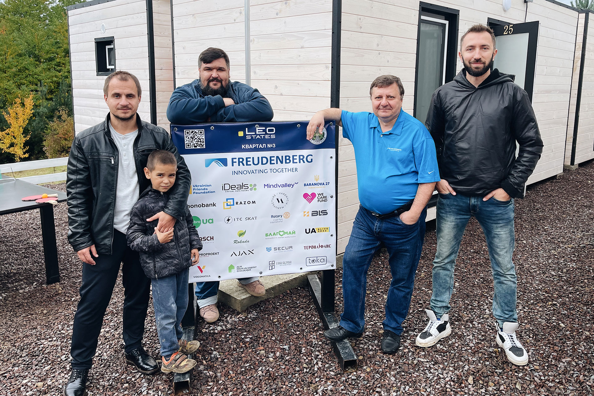Eine Gruppe von fünf Personen vor einem Containerdorf 