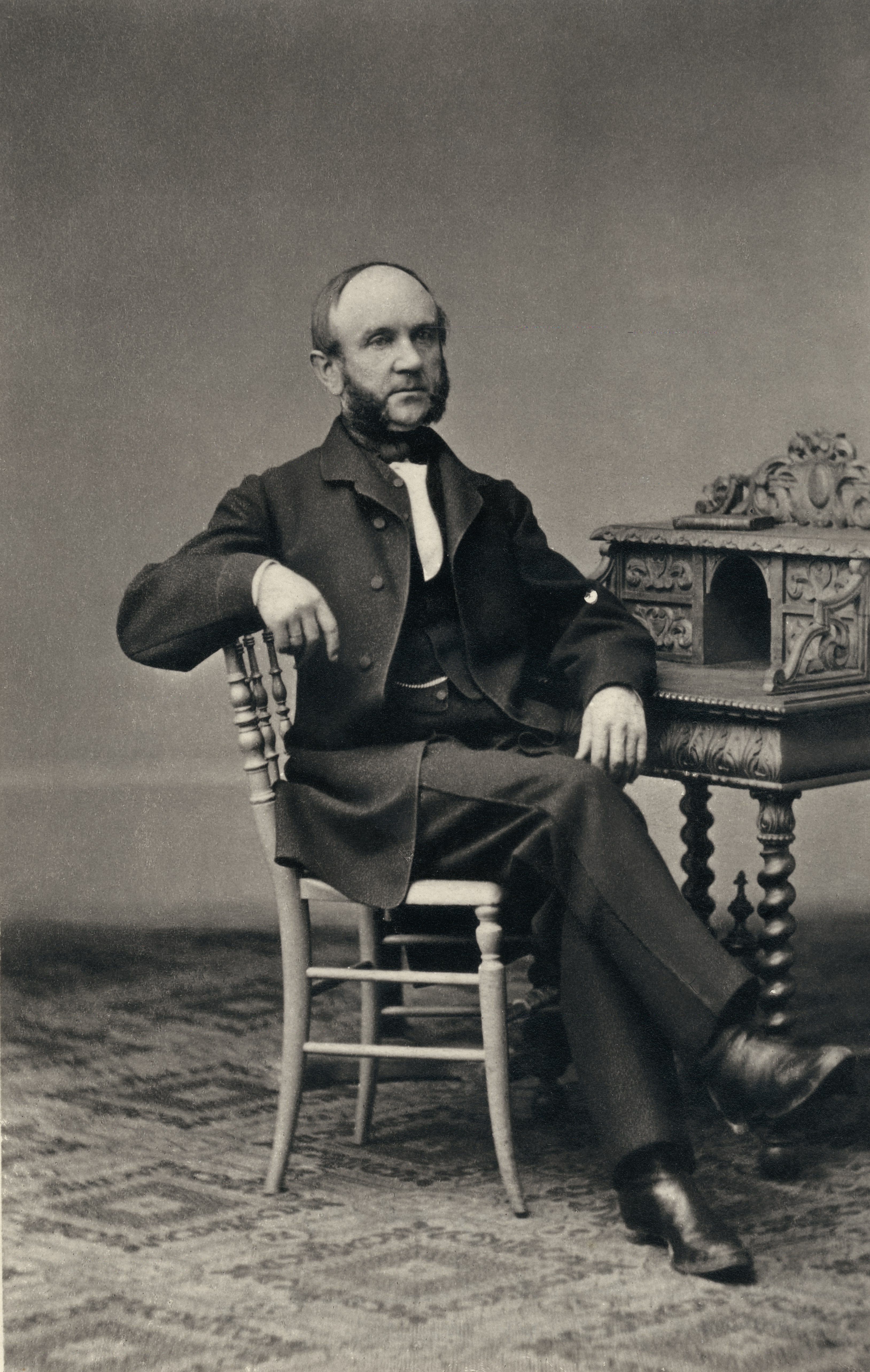 Picture shows portrait of a man who is wearing a suit and is sitting on a chair