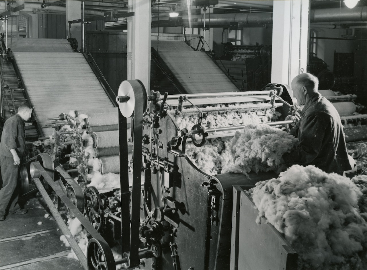 Picture shows a factory from the inside where two men are working on a machine that produces nonwoven
