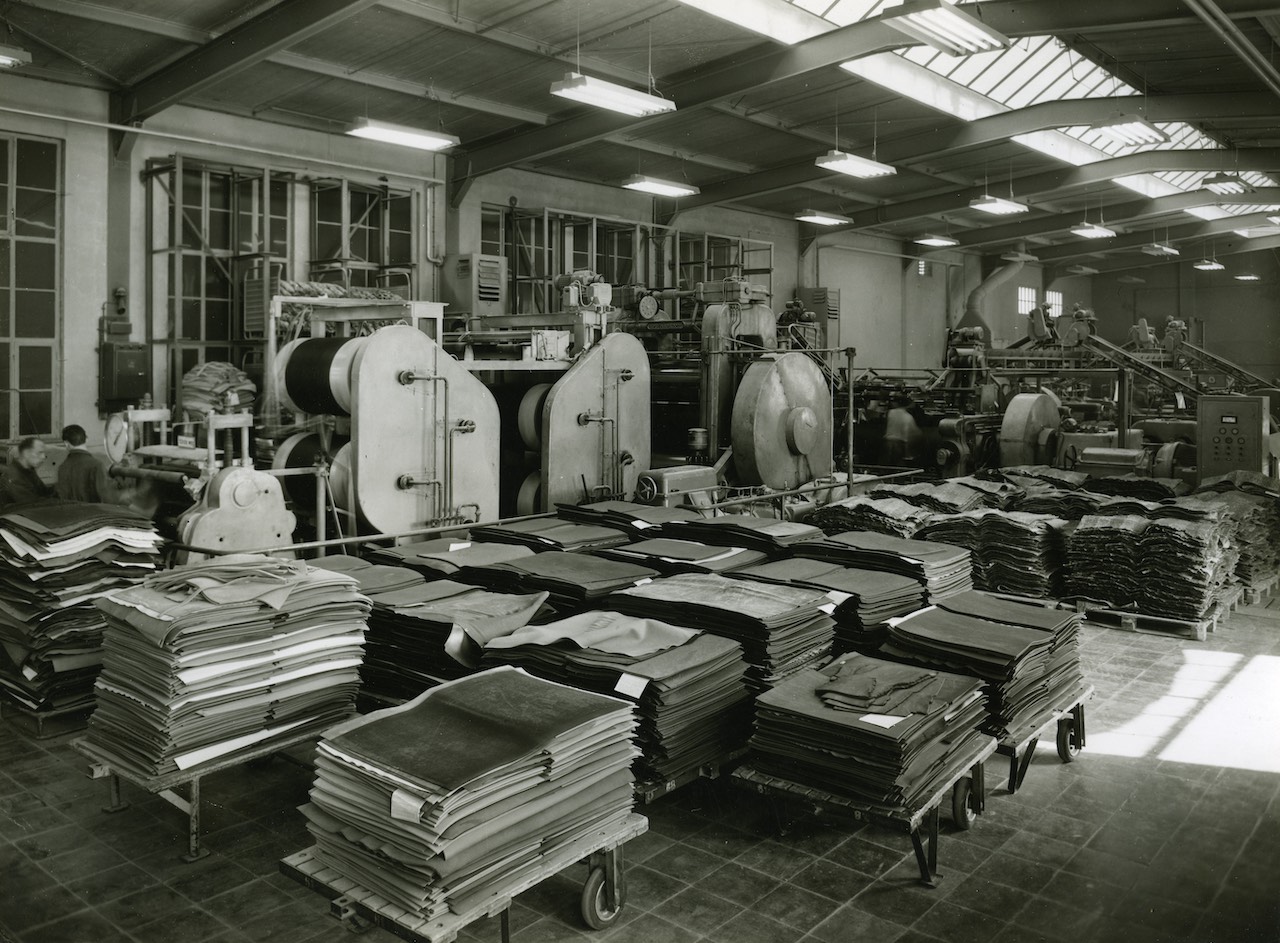 Picture shows a large room that looks like the inside of a factory. The room is filled with floor coverings which are stapled on top of each other