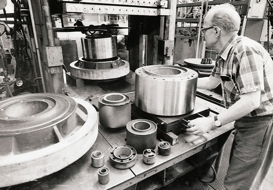 The picture shows an elderly man wearing casual clothes and working on a machine that produces vibration control ultra bushings
