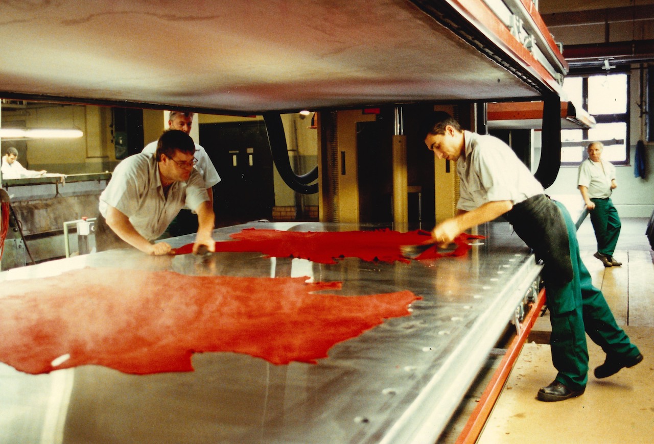 Picture shows two men working on a metal table that is covered with red leather