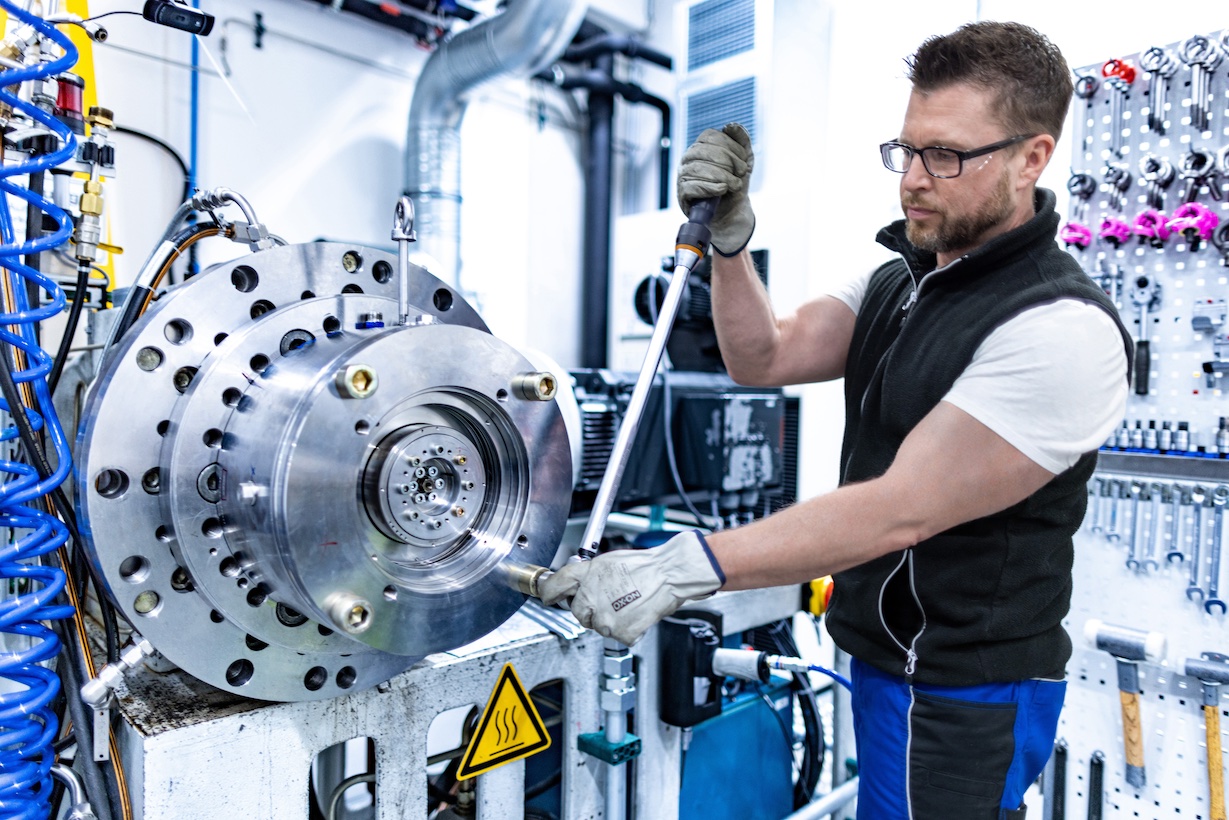 A man wearing blue collar gear is working on a large mechanical seal