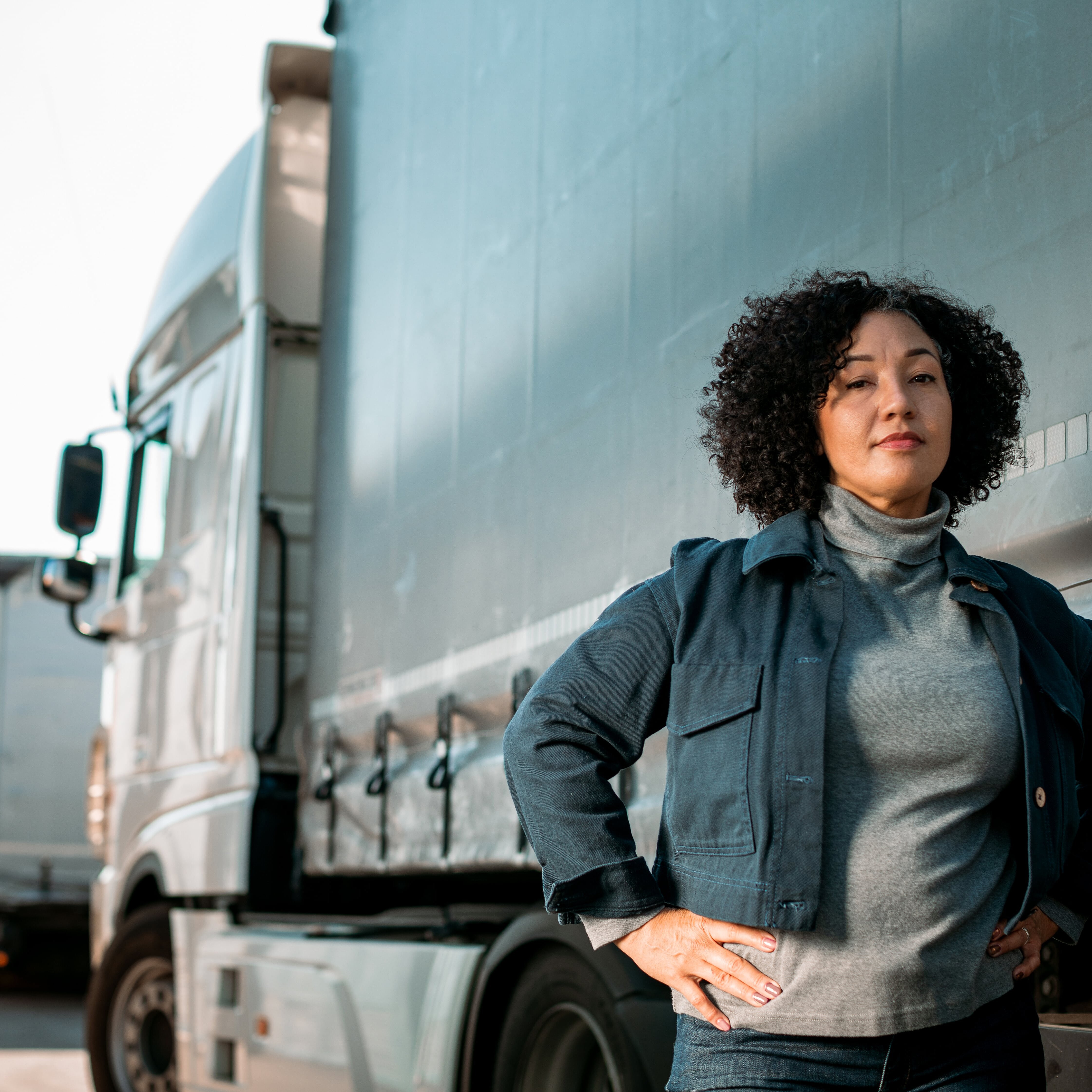 a woman with back curly hair standing in front of big truck