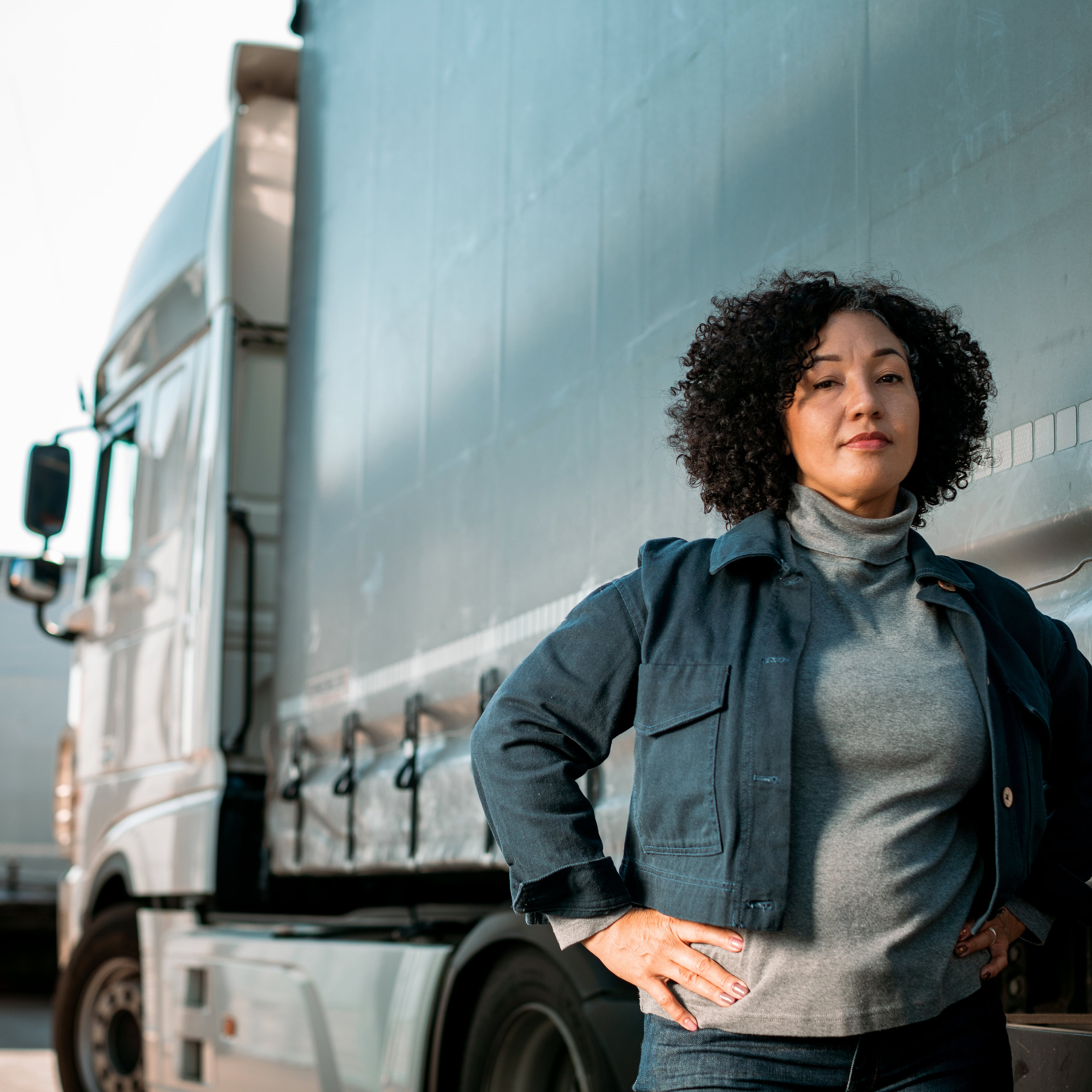 a woman with back curly hair standing in front of big truck