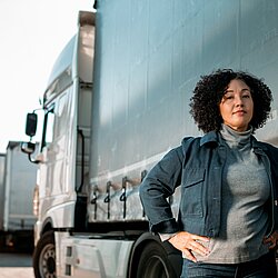 a woman with back curly hair standing in front of big truck