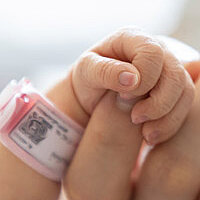 a tiny baby hand grabbing one finger of an adult hand