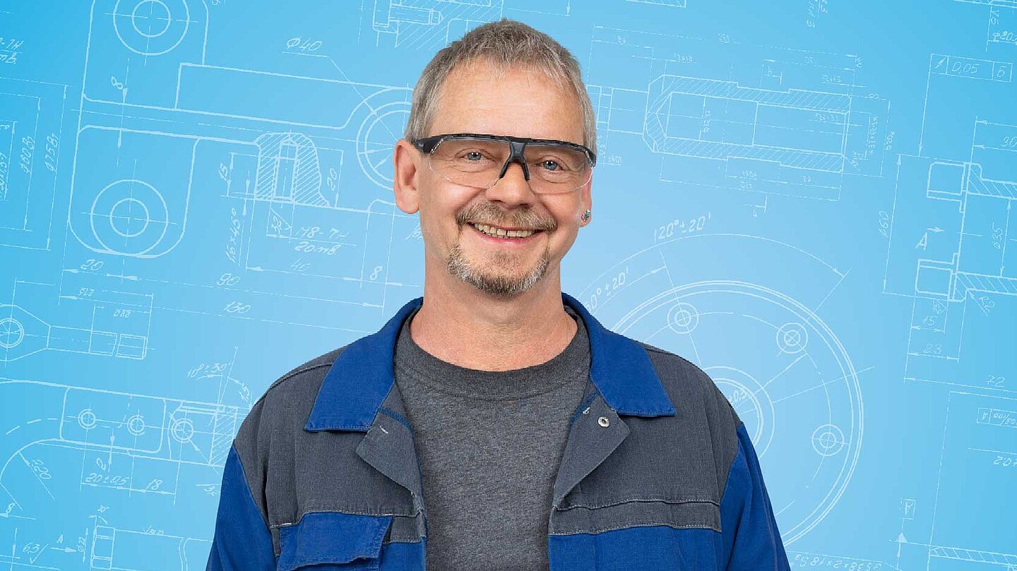 Portrait einer männlichen Person, die in der Bildmitte vor einem blauen Hintergrund abgebildet ist.