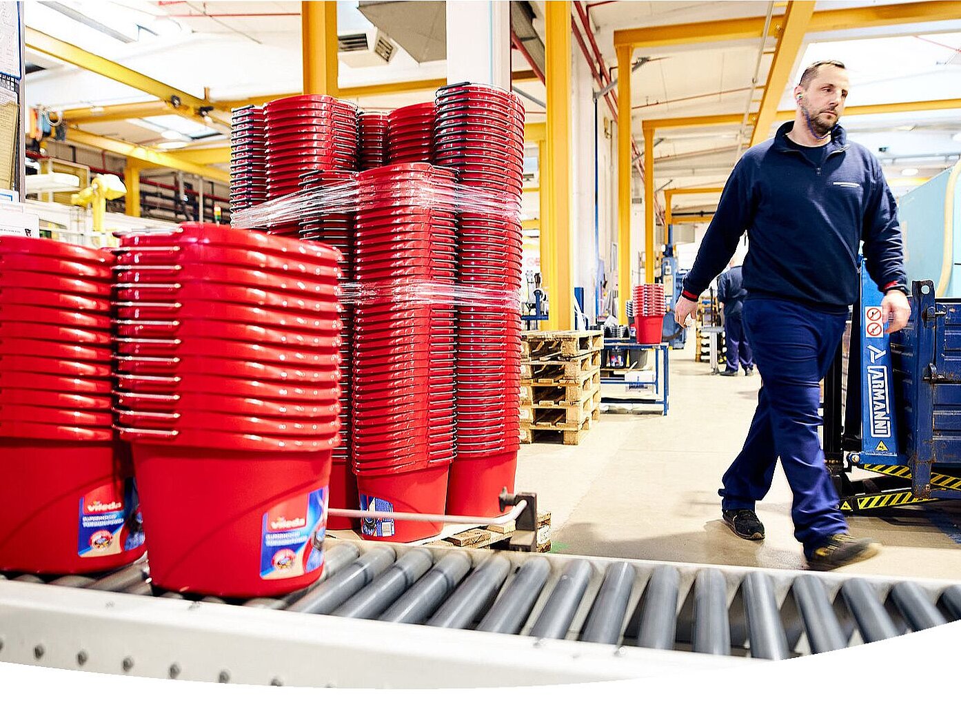 A man in a manufacturing hall walking next to hundreds of red Vileda buckets