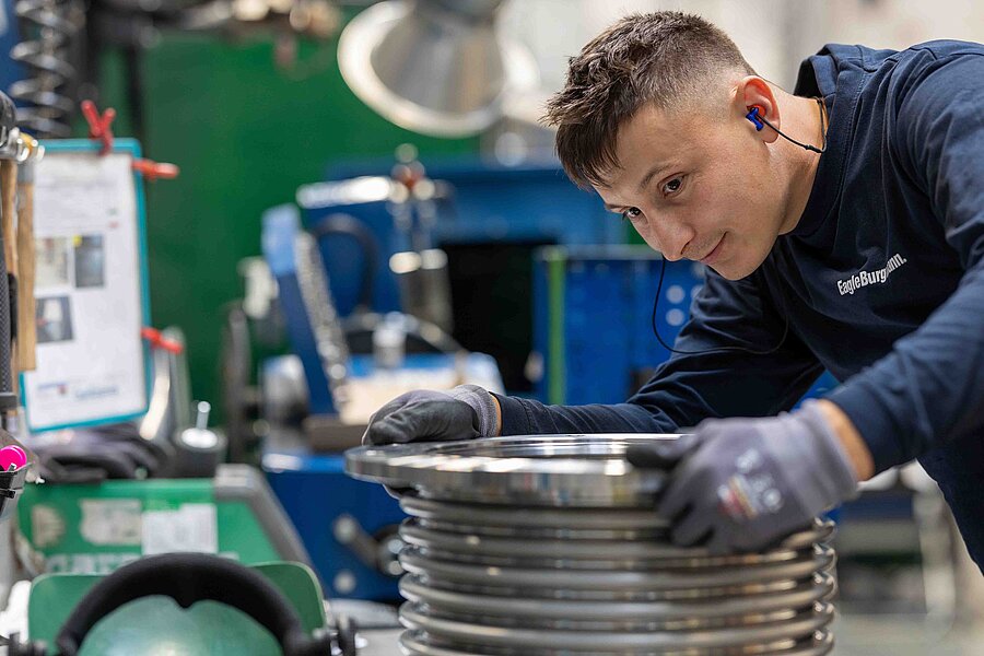 The picture shows a man in a workshop working on a round object