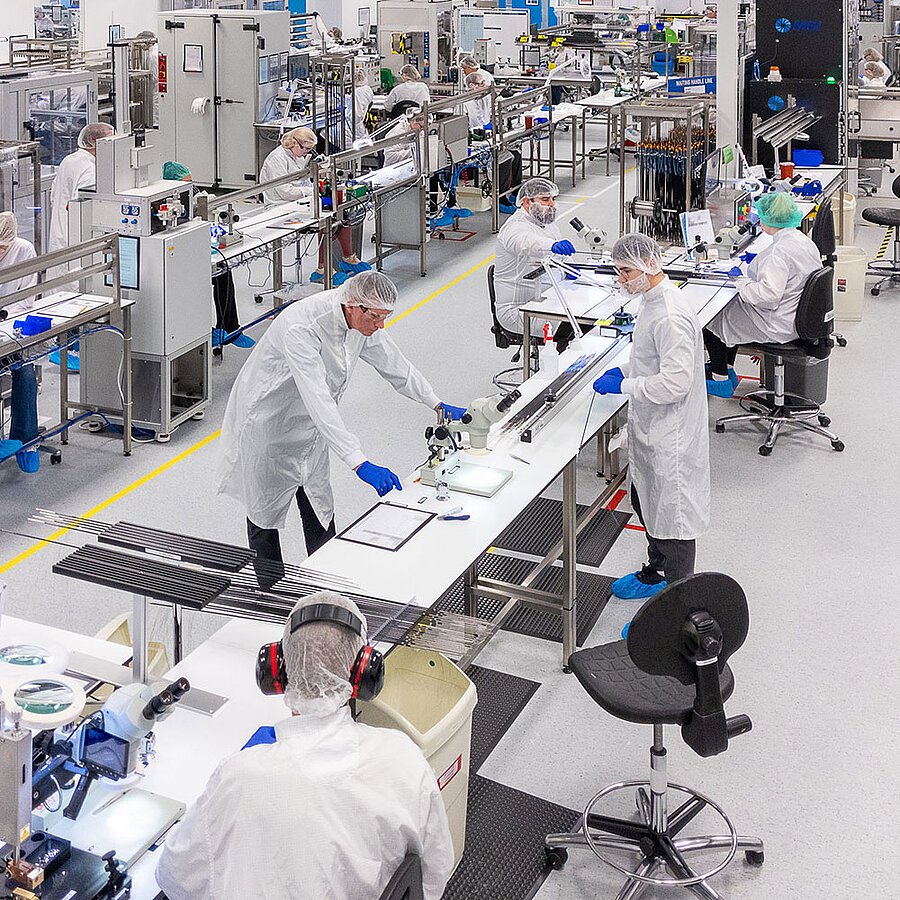 Employees working at a production line in a cleanroom manufacturing environment.