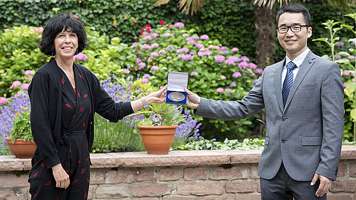 Eine Frau überreicht einem Mann eine Medaille in einer kleinen Schachtel.