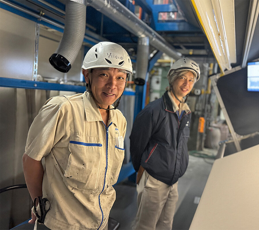 Two people wearing work clothes and white safety helmets smiling into the camera