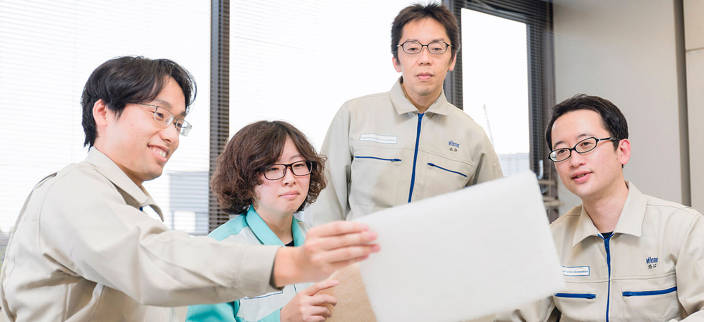 The photo shows a woman and three men sitting next to each other, all looking at a white, sqaure item one of the men is holding