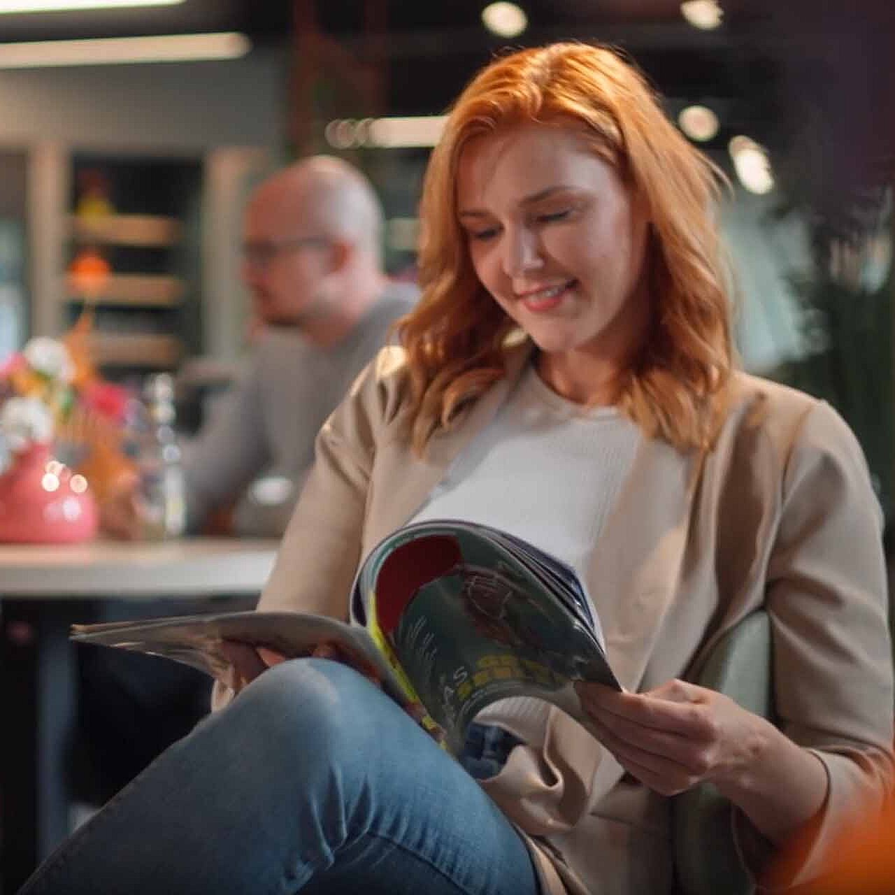 A young woman sitting in a coffee shop and is reading in a magazine