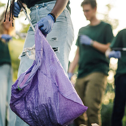 Close-up of a purple garbage bag held by a person who appears to be collecting more garbage