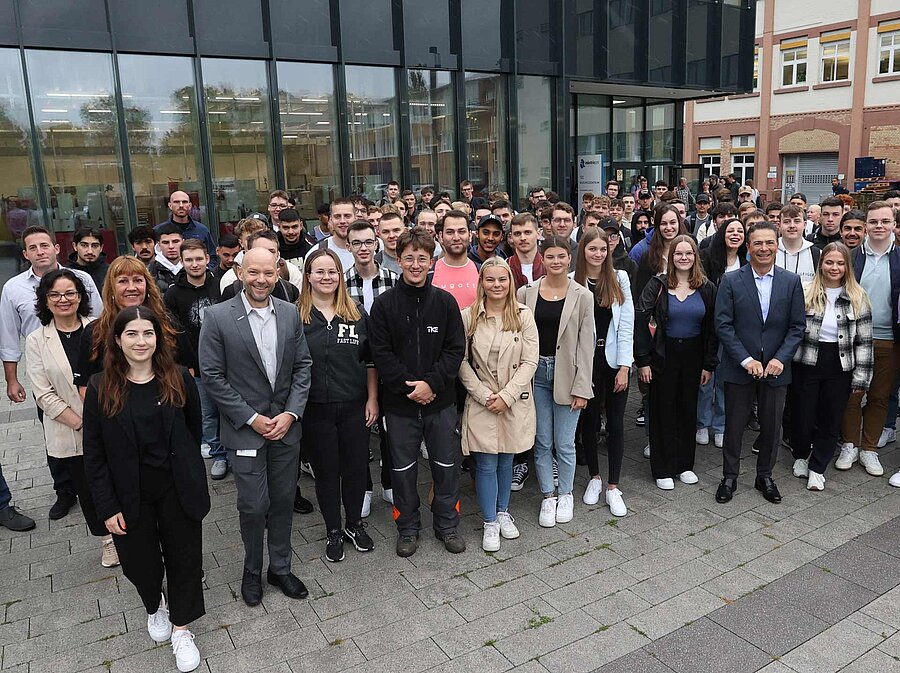 Das Bild zeigt eine große Gruppe von Menschen, die vor einem Gebäude stehen und in die Kamera lächeln