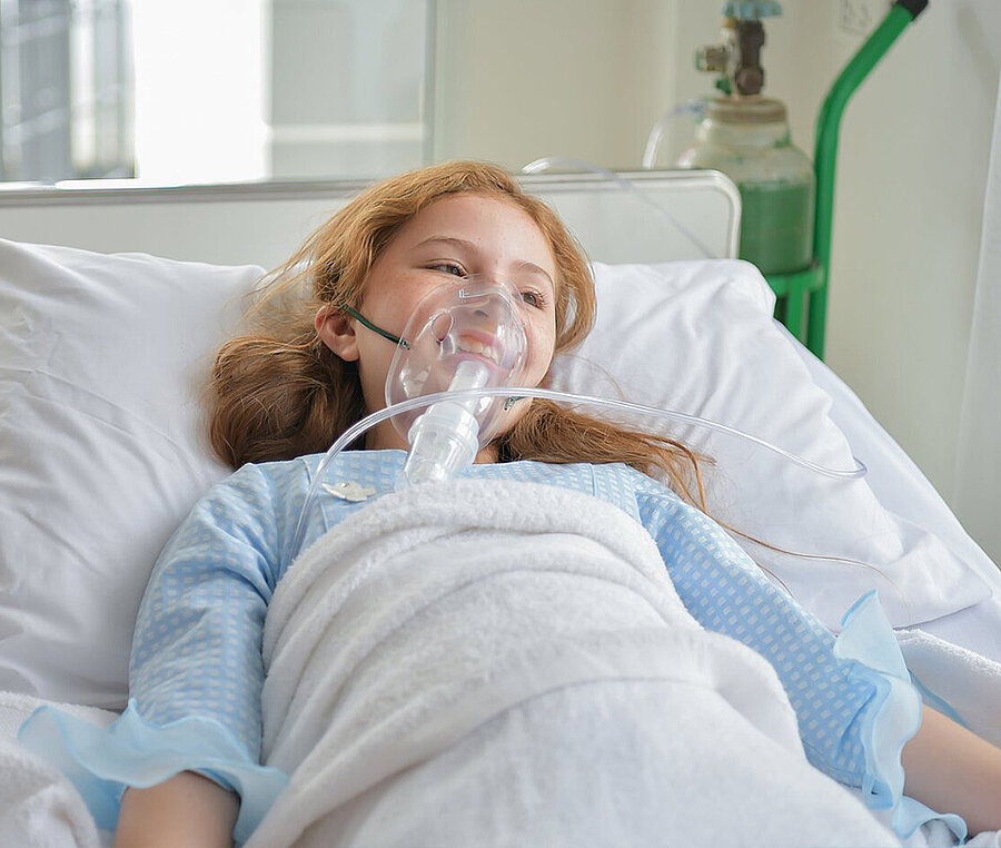 A girl in a hospital bed with an oxygen mask