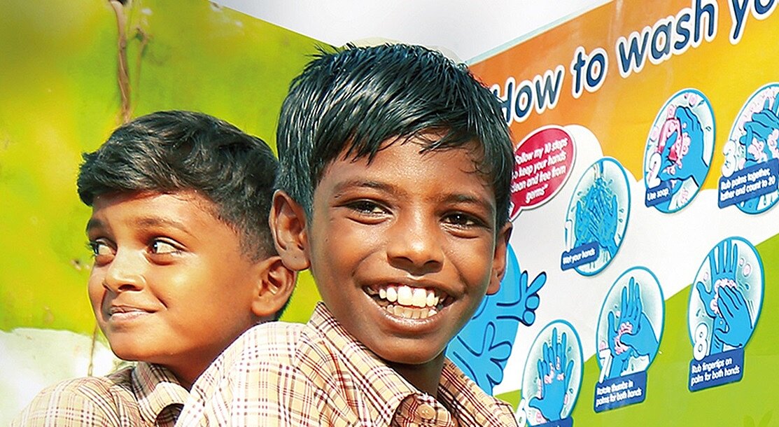 Two Indian boys standing in front of a sign that explains how to wash your hands properly