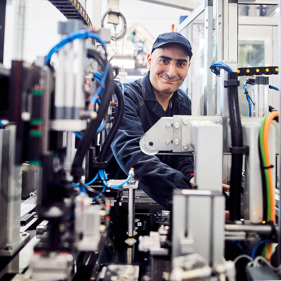 Worker operating an industrial machine in a manufacturing environment and looking friendly at the camera.
