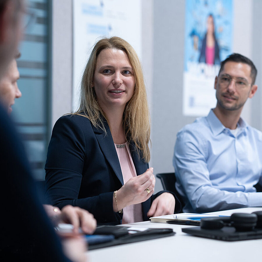 Three people are sitting in a meeting room talking to each other.