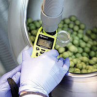gloved hands hold a measuring device in a round steel container with green beads