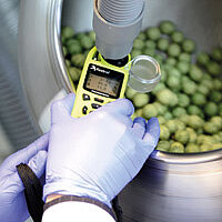 gloved hands hold a measuring device in a round steel container with green beads
