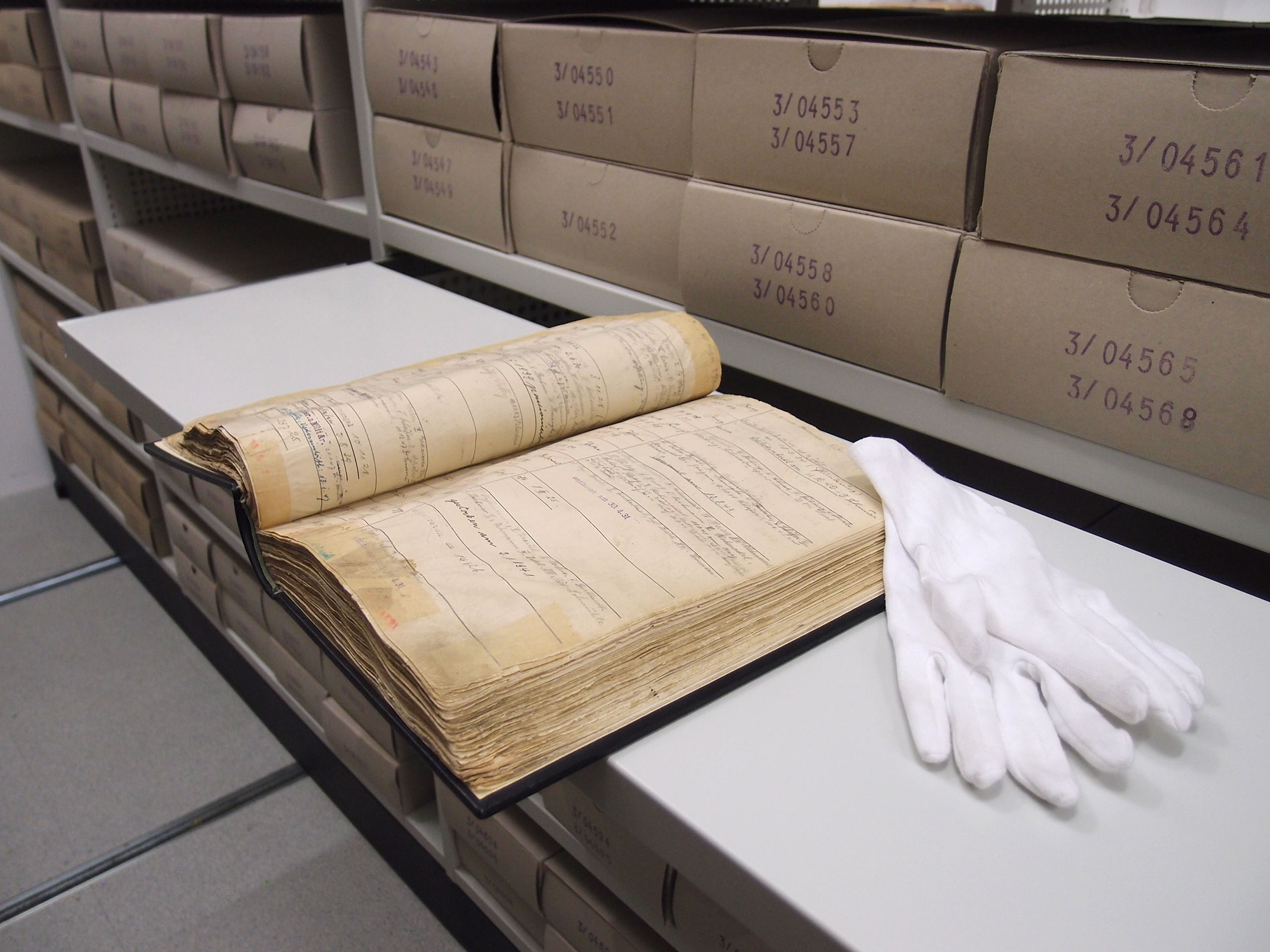 Mitarbeitendenverzeichnis aus dem 19. Jahrhundert. Weiße Handschuhe liegen rechts daneben.
