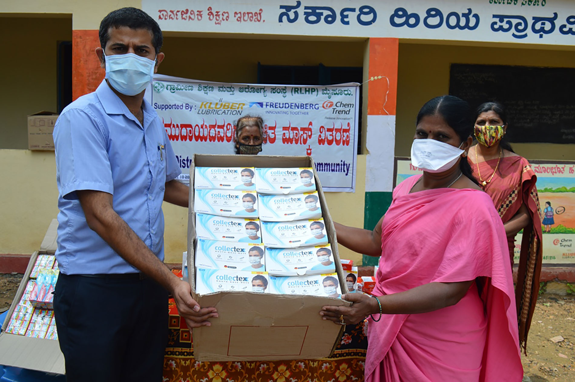 A man and a woman hold a large cardboard box containing donated Freudenberg face masks.