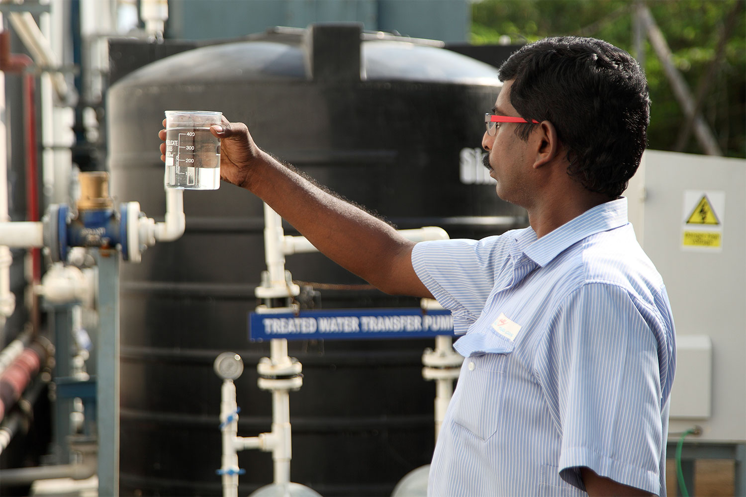 Mann hält ein Glas Wasser hoch und prüft Qualität des gereinigten Abwassers